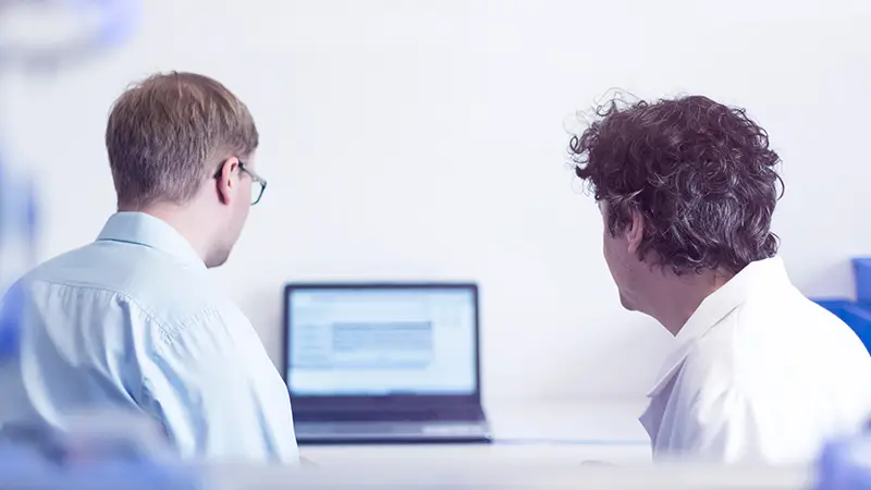 Zwei Mitarbeiter besprechen technische Details an einem Laptop